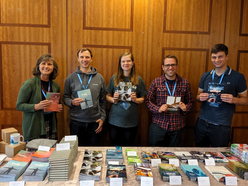 A bookstall with five people behind holding a book each.